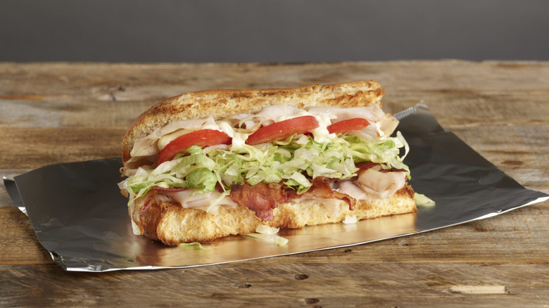 A Turkey Club sits on a piece of foil on a wooden table