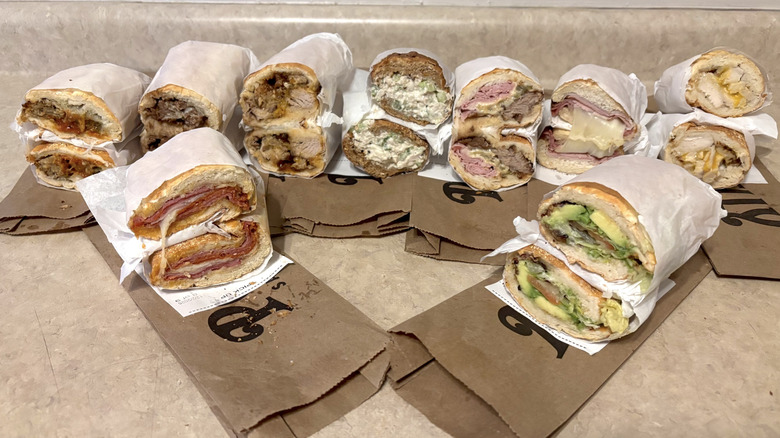 A variety of Potbelly sandwiches, wrapped in paper, on neutral counter