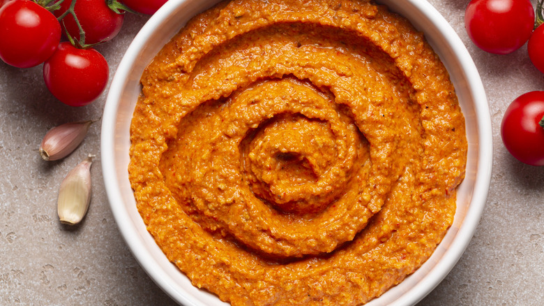 romesco sauce in a bowl with garlic and tomato kept around it