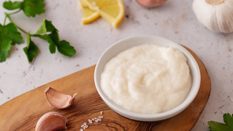 toum sauce in a bowl with garlic cilantro lemon on the table around it