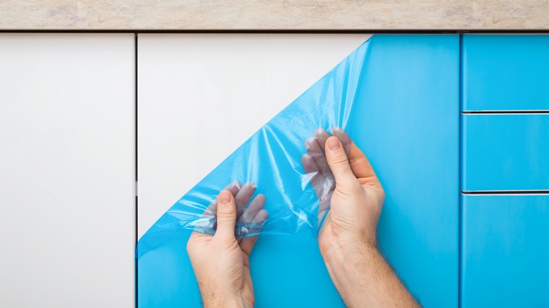 a person peeling blue plastic film off a cabinet door