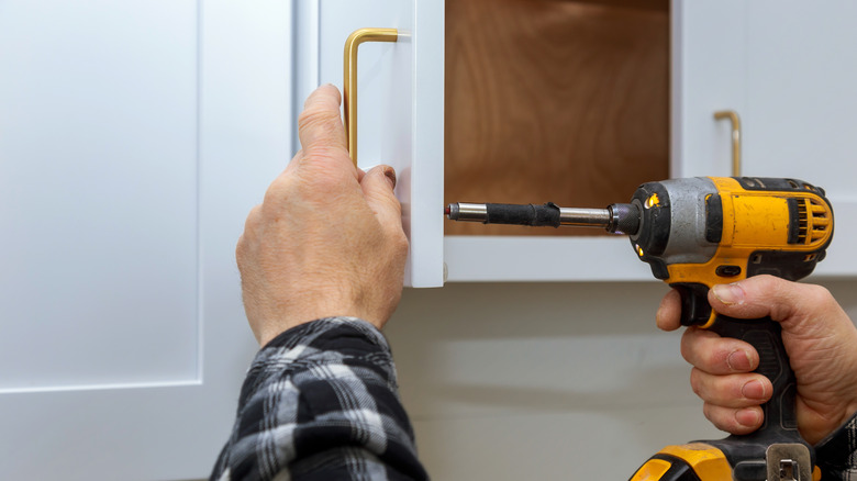 person installing a cabinet door handle with a drill
