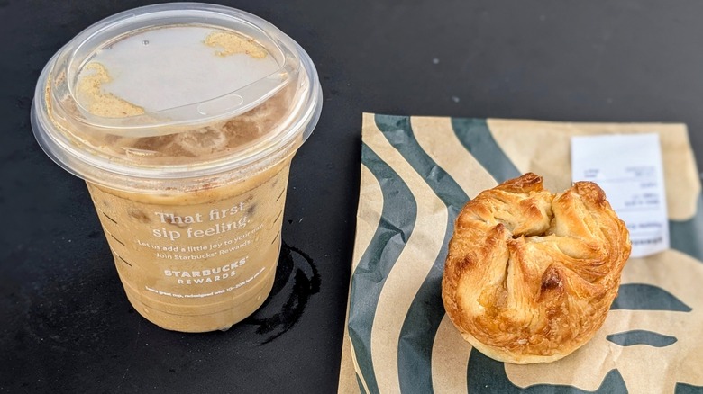 Iced Brown Sugar Shaken Espresso next to a small, round croissant on a black table