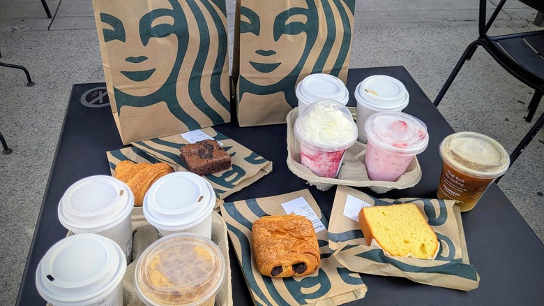 Various Starbucks drinks and pasteries next to Starbucks paper bags on a black table outside