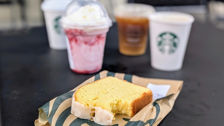 A lemon loaf with a bite taken out and various Starbucks drinks in the background