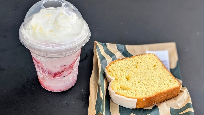 A strawberry Frappuccino next to a yellow iced loaf slice on a black table