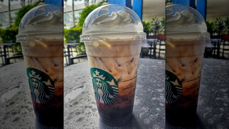 Starbucks Iced Americano with whipped cream topping, in lidded branded cup on table