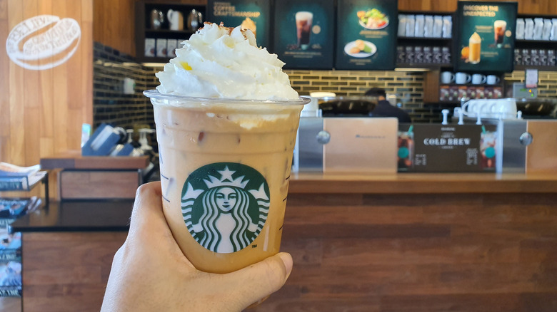 Hand holding Starbucks iced pumpkin drink, topped with whipped cream