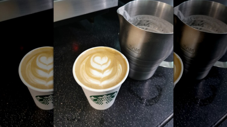 Pumpkin flat white in Starbucks cup next to metal milk pitcher