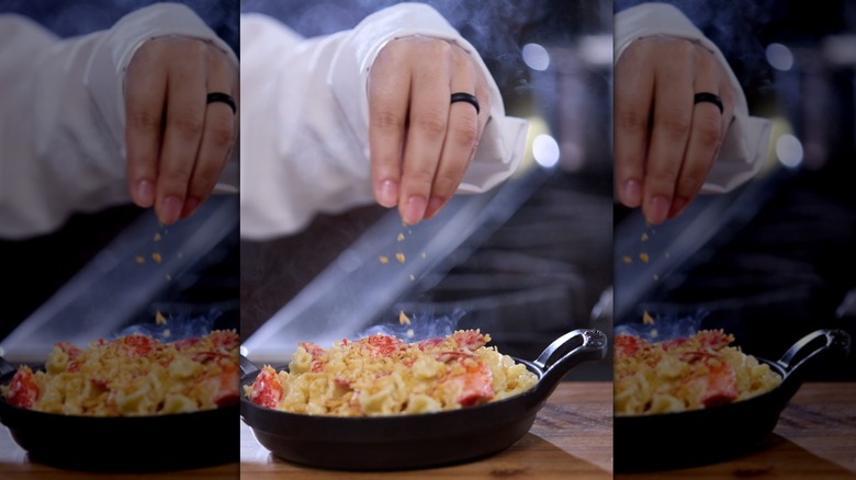 Hand sprinkling garnish onto lobster mac and cheese