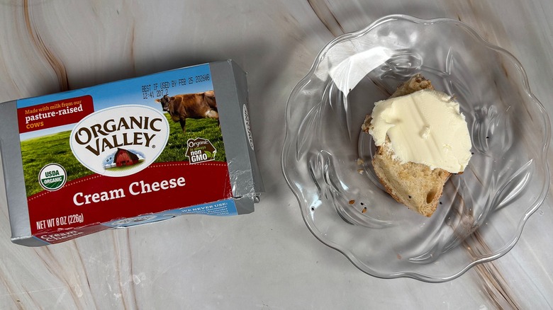 Package of Organic Valley cream cheese next to bagel piece with cream cheese on glass plate