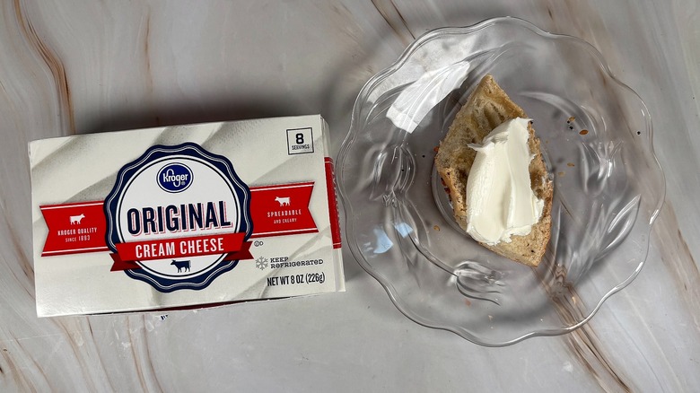 Package of Kroger cream cheese next to bagel piece with cream cheese on glass plate