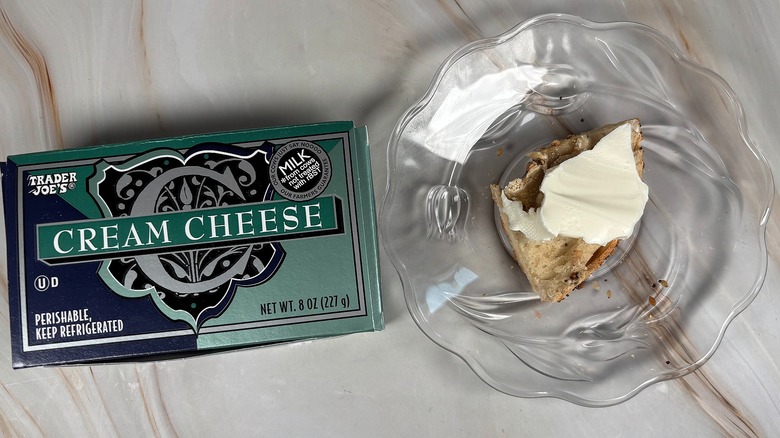 Package of Trader Joe's cream cheese next to bagel piece with cream cheese on glass plate