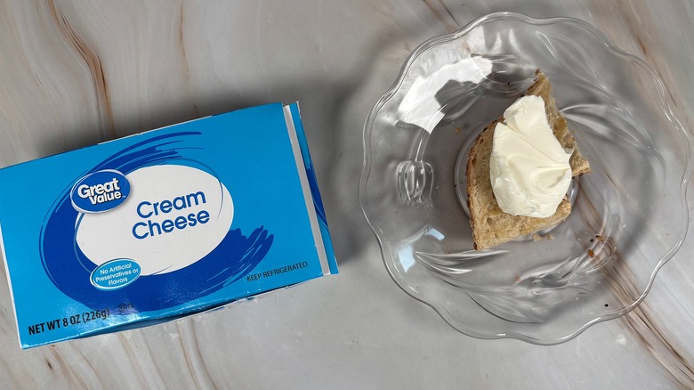 Package of Great Value cream cheese next to bagel piece with cream cheese on glass plate