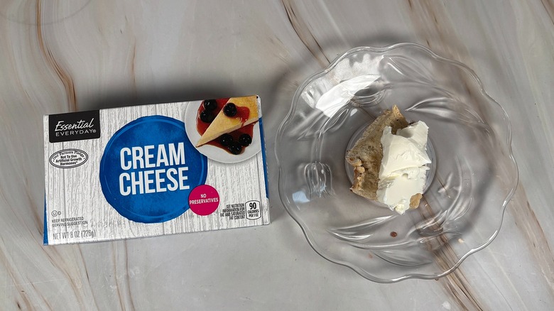 Package of Essential Everyday cream cheese next to bagel piece with cream cheese on glass plate