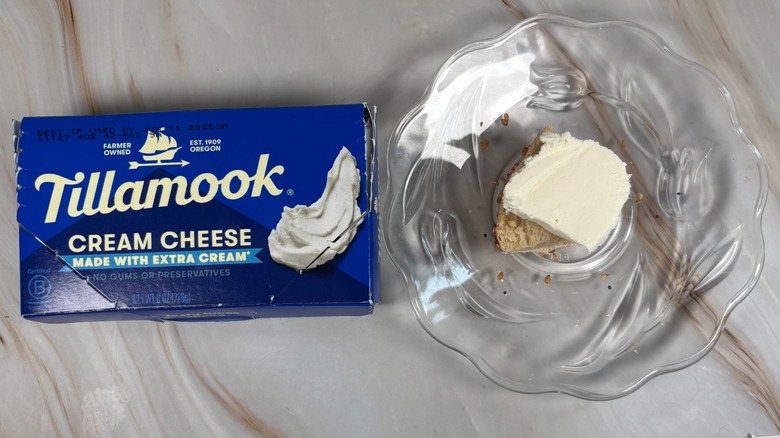 Package of Tillamook cream cheese next to bagel piece with cream cheese on glass plate