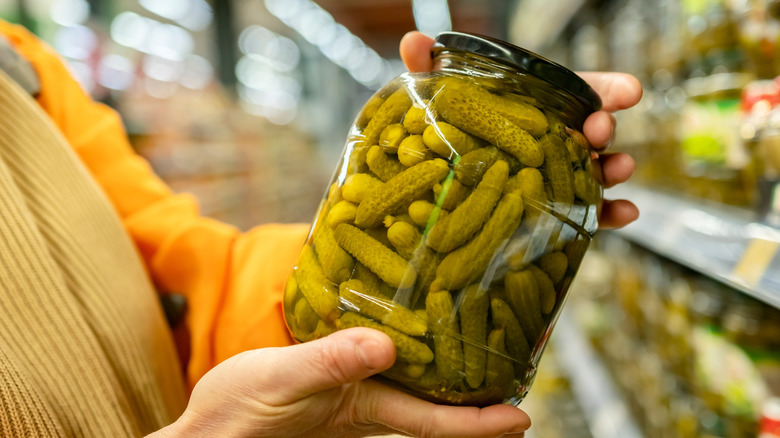 Person holding a jar of pickles in a grocery store