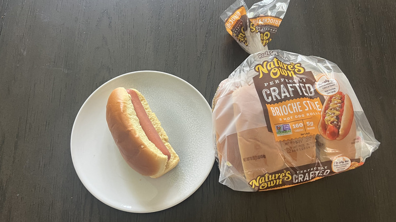 Nature's Own Brioche Style Hot Dog Roll packet with one hot dog assembled and served on a white plate