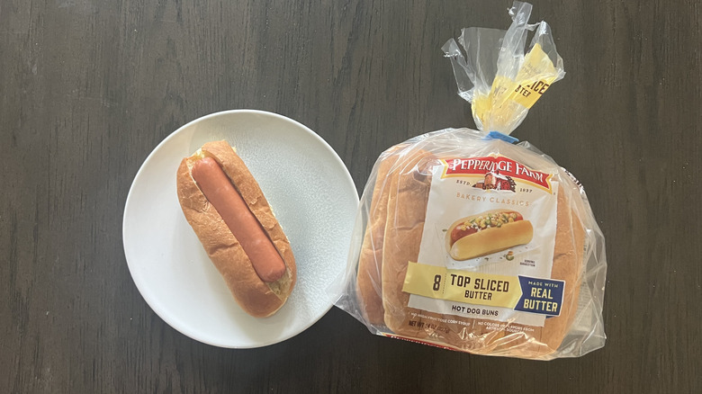 A packet of Pepperidge Farm Top-Sliced Butter Hot Dog Bun with one prepped hot dog on a white plate