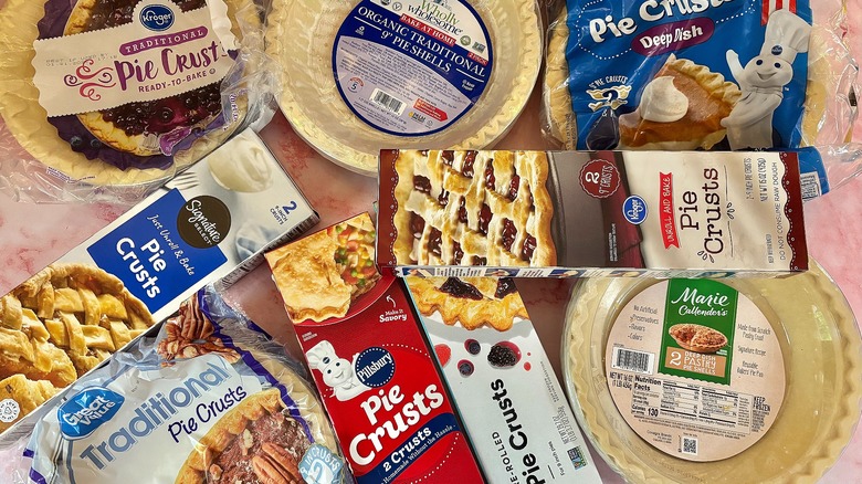 Several refrigerated and frozen pie crusts in packaging on pink marble surface