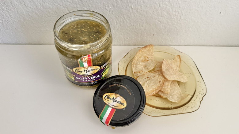 A jar of Casa Martinez Fire-Roasted Salsa Verde Tatemada served with chips on a plate