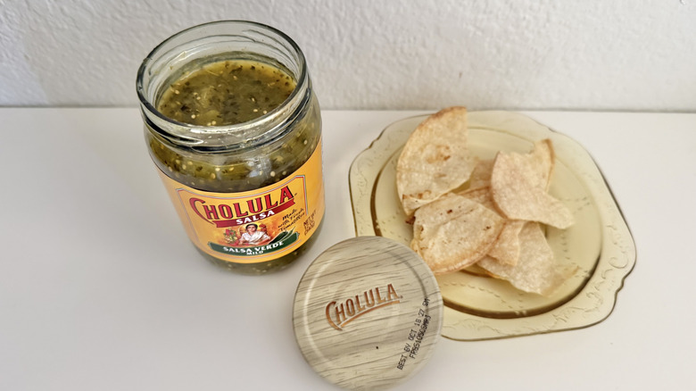 Cholula Salsa Verde lid and jar on a table with some tortilla chips on a plate