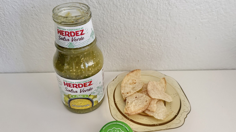 Herdez Salsa Verde jar on a white table served with chips