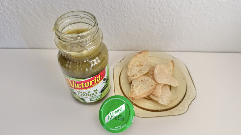 Open jar of La Victoria Salsa Verde on a table with chips on a plate