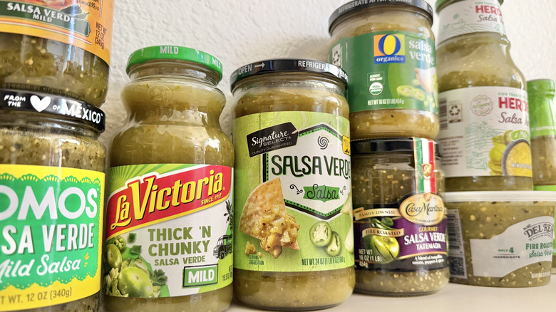 Close up of various jarred salsa verde brands on a table