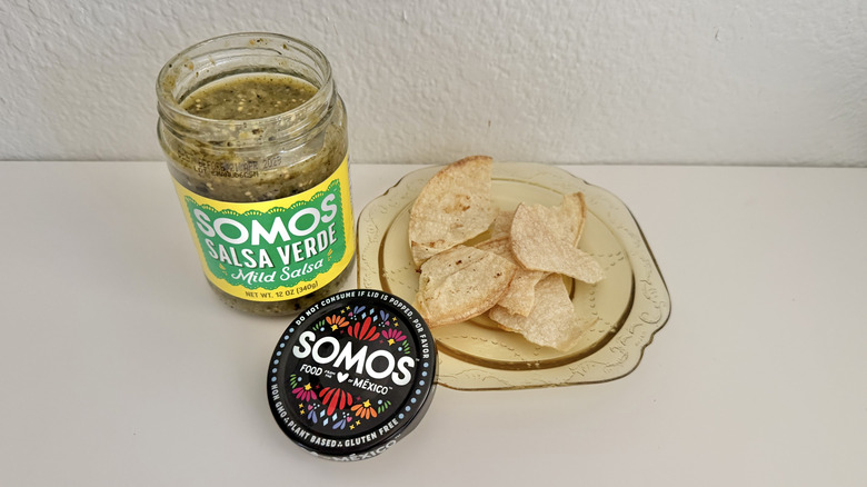 Tortilla chips on a plate with a jar of Somos Mild Salsa Verde