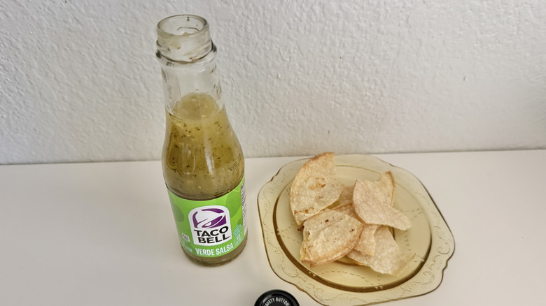 Bottle of Taco Bell Verde Salsa opened on a white table with tortilla chips
