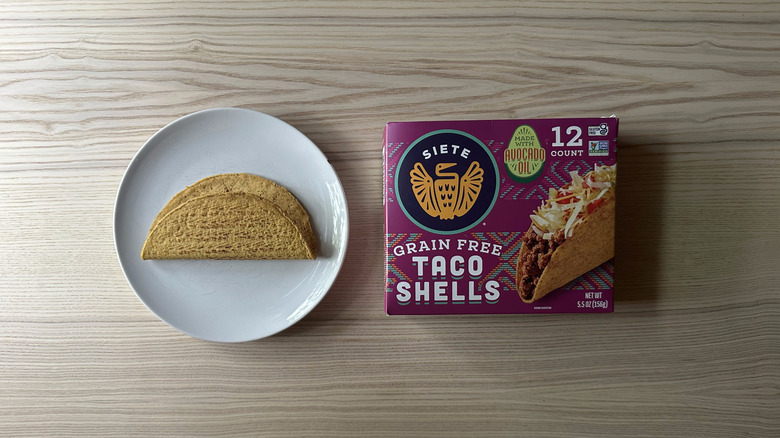 A box of Siete Grain Free Taco Shells on a wooden table with one shell on the plate next to it
