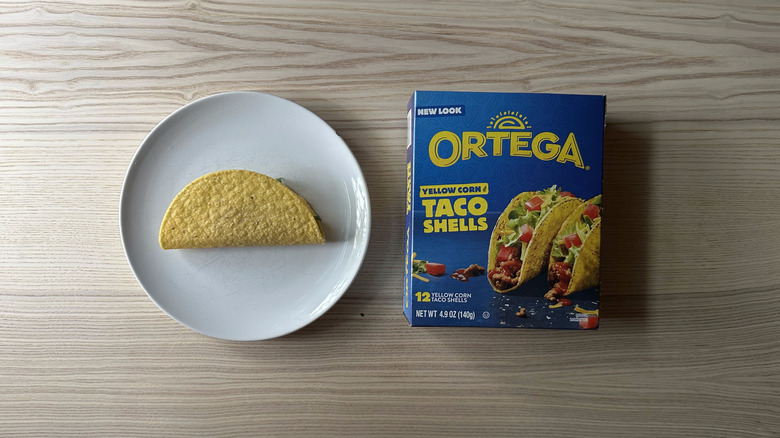 A plate with a taco shell and Ortega Yellow Corn Taco Shells box on wooden table