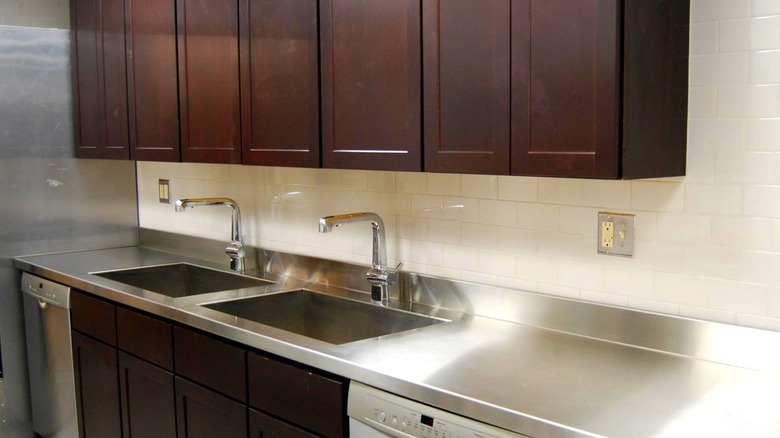 Row of dark wood cabinets above stainless steel countertop with white tile wall