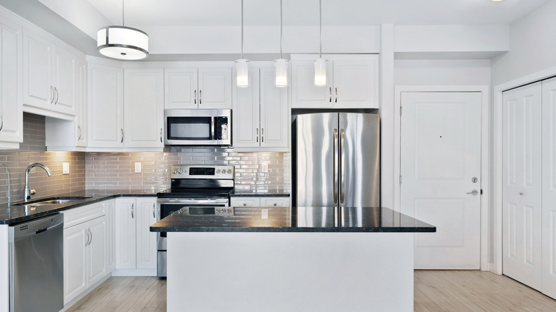 White kitchen with stainless steel counters, steel fridge, and tile backsplash