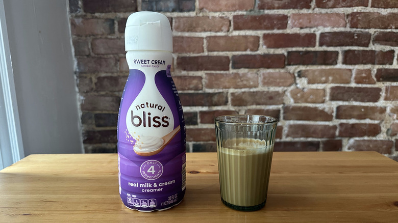 Natural Bliss Sweet Cream Coffee Creamer and cup of coffee on wooden table with brick background