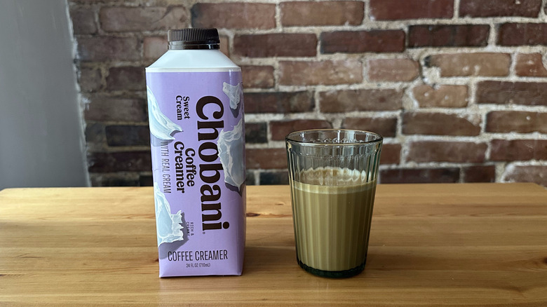 Chobani Sweet Cream Coffee Creamer and cup of coffee on wooden table with brick background