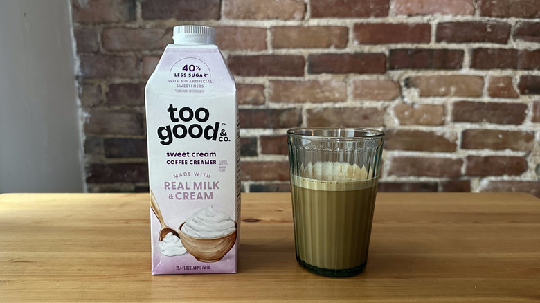 Too Good & Co. Sweet Cream Coffee Creamer and cup of coffee on wooden table with brick background