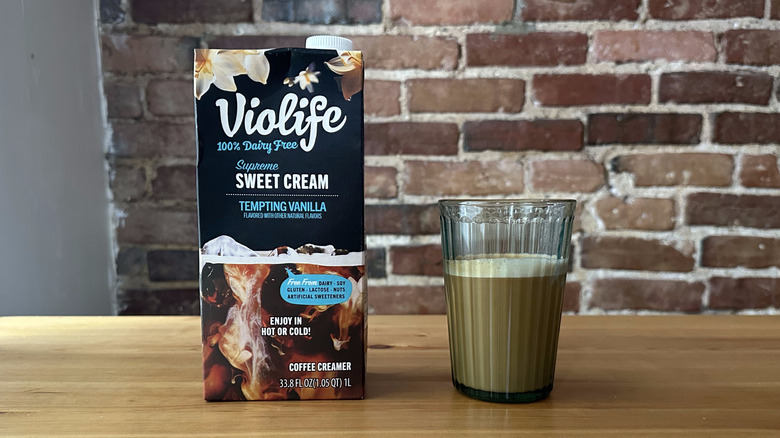 Violife Supreme Sweet Cream Tempting Vanilla Coffee Creamer and a cup of coffee on wooden table with a brick background