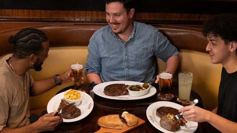 Three men sitting at a table at LongHorn Steakhouse eating steak and sides.