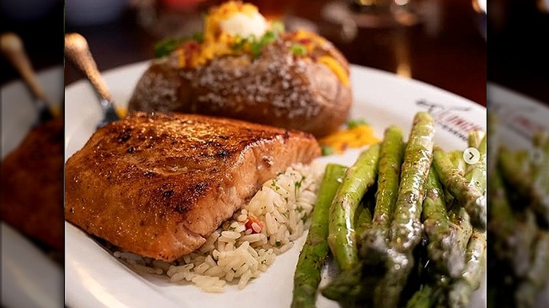 Plate of salmon over rice with a side of asparagus and loaded baked potato.