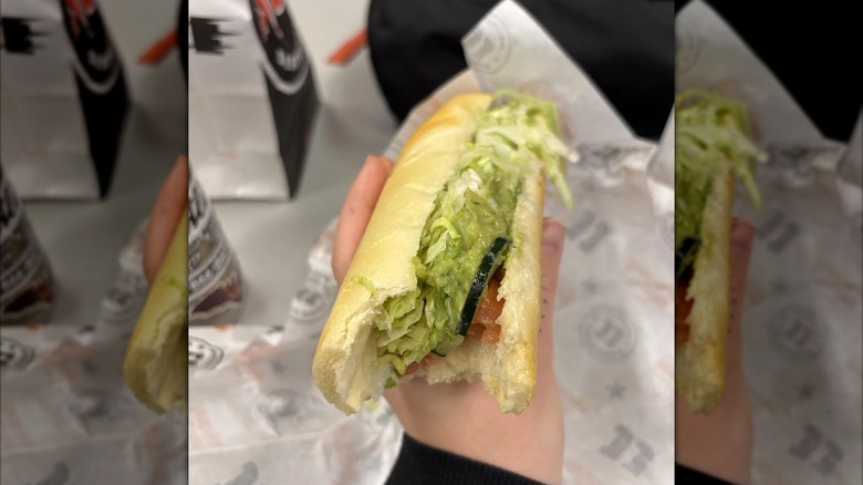 Mirrored image of hand holding salad sandwich over Jimmy John's packaging