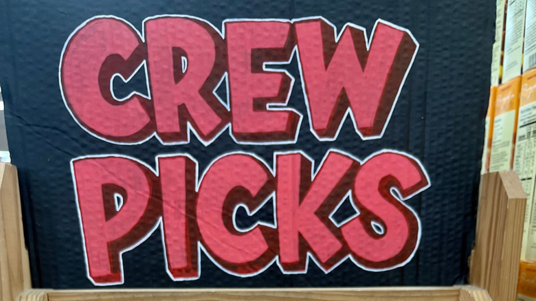 Person holding an item in front of a "Crew Picks" sign