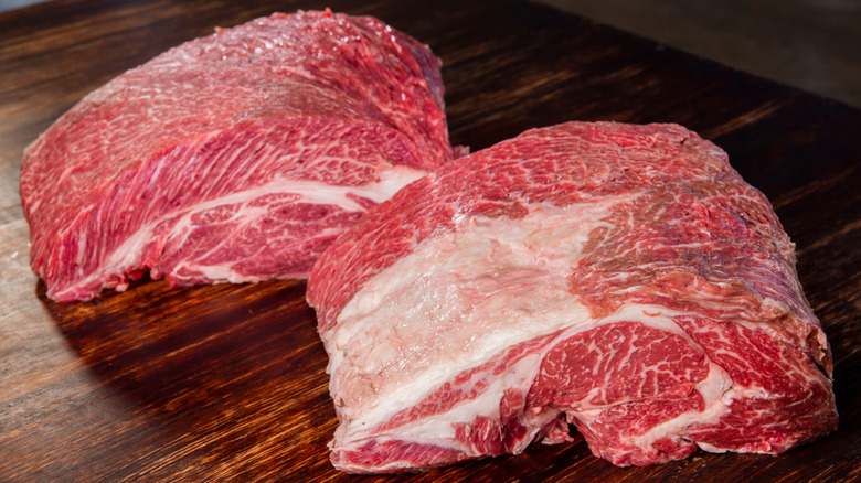 Two large raw chuck roasts side by side on wood surface.
