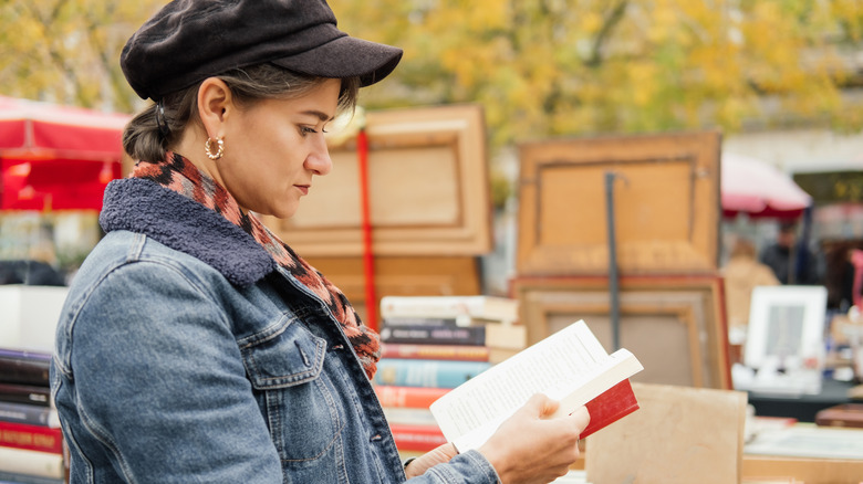 Woman in a black hat and blue jacket looking at a book at an outdoor flea market