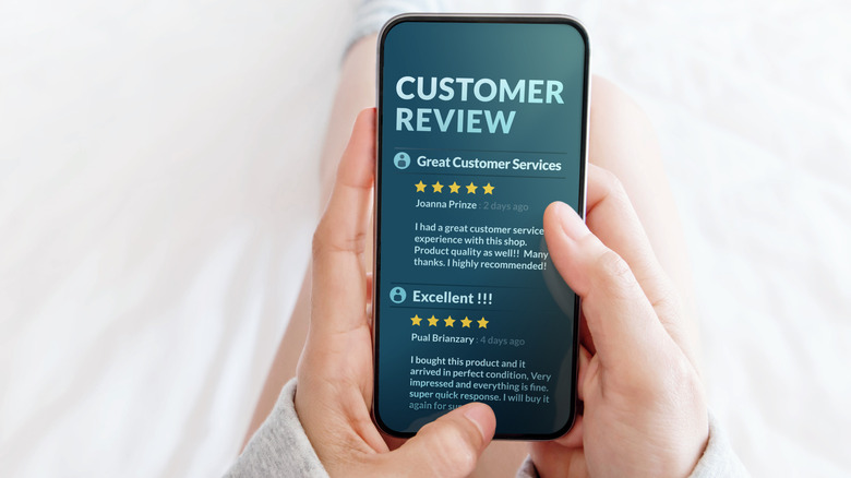 A woman holding her phone and looking at different 5 star customer reviews.