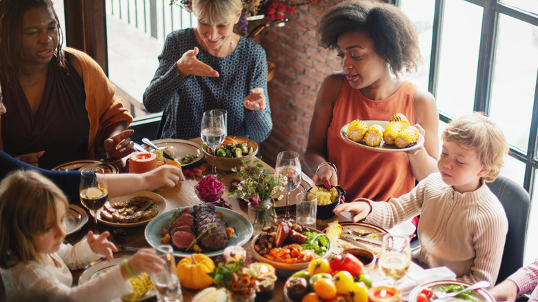 A group of friends and kids gathered around a dinner table full of food.