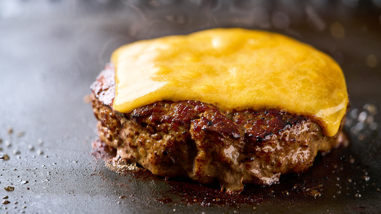 Slice of melted American cheese on single burger patty
