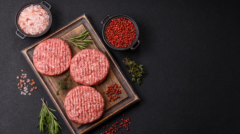 Burger patties on wooden board surrounded by different spices in bowls