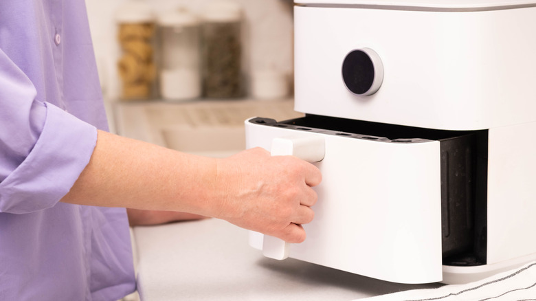 Hand pulling white air fryer basket out of machine